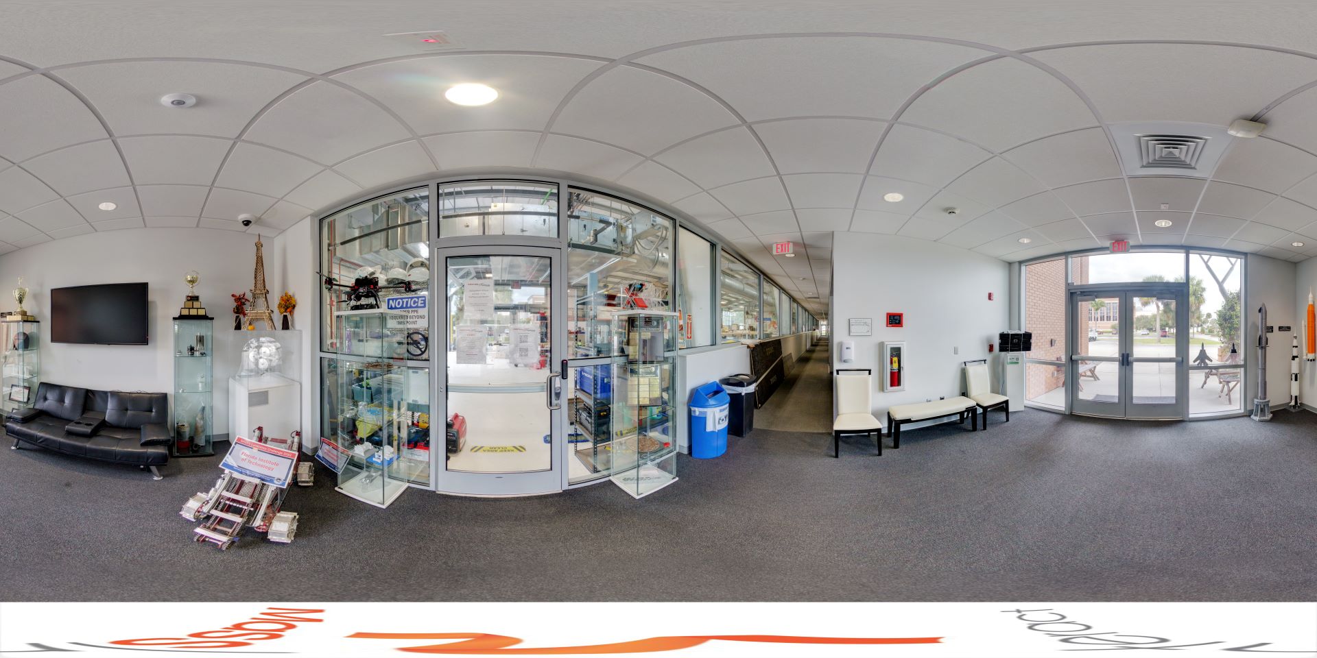 Panoramic view of a lobby featuring a curved ceiling, display cases with trophies and models, and a clear view of an adjoining lab through glass doors